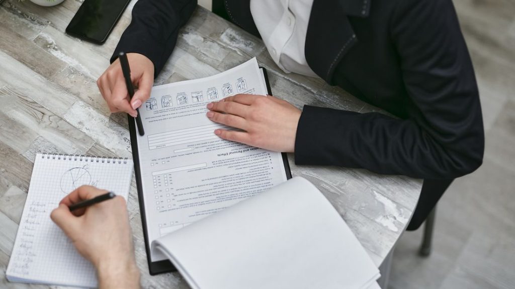 Two colleagues reviewing documents and taking notes during a meeting