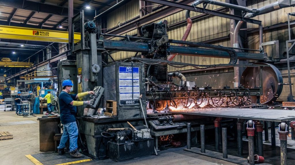 A worker in safety gear operating machinery on a manufacturing floor
