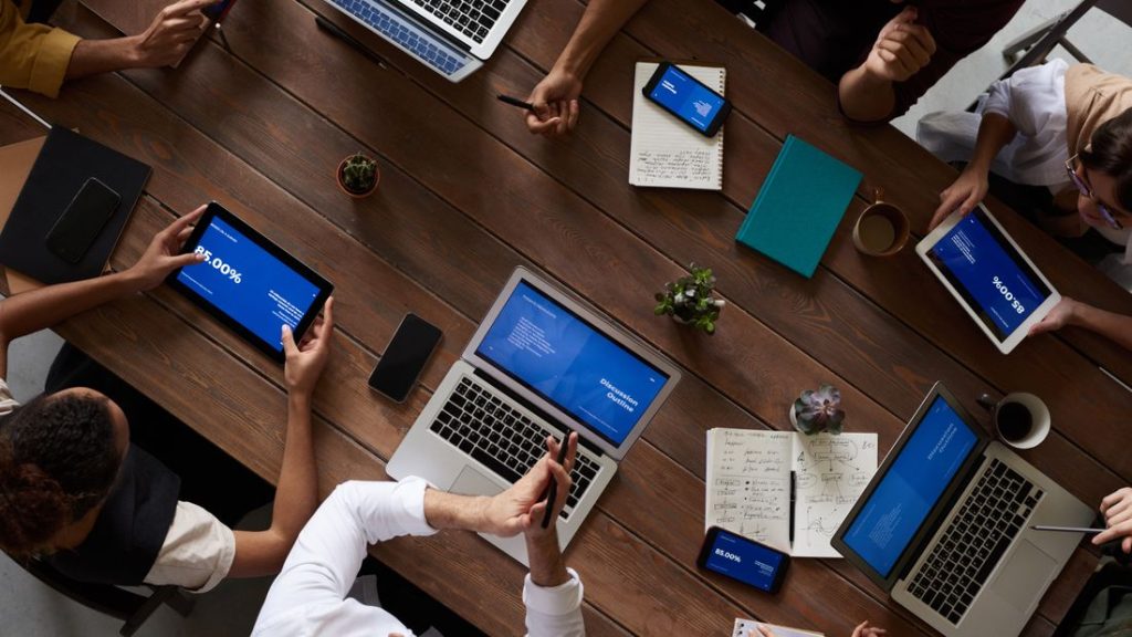 Overhead view of a team analysing figures on laptops around a wooden table